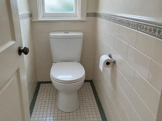 Clean white toilet in a tiled small bathroom with window and paper holder in Brighton-Le-Sands