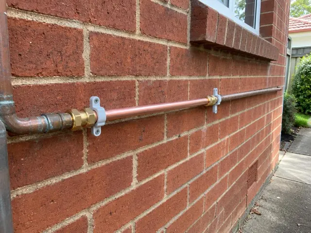 Repaired copper water pipe on a red brick exterior wall in Arncliffe